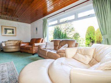 A living room with multiple leather sofas green curtains and large window at Trevow Camborne