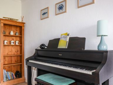 A dark piano with sheet music and headphones next to a wooden bookshelf with ceramics and books at Trevow Camborne