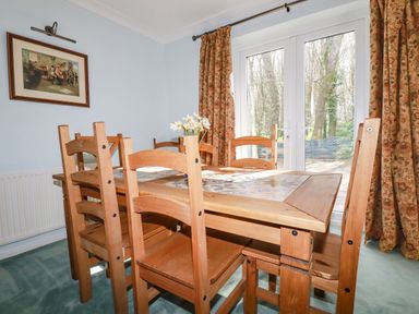 A dining room with a wooden table and chairs near glass doors with floral curtains at Trevow Camborne