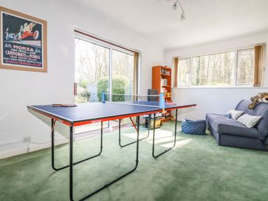 A room with a ping pong table a blue sofa a bookshelf and windows at Trevow Camborne