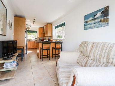 A kitchen and living area with a striped sofa a wooden kitchen island with chairs and a small TV on a stand at Trevow in Camborne