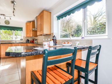 A kitchen with wooden cabinets and two chairs at a black countertop at Trevow in Camborne