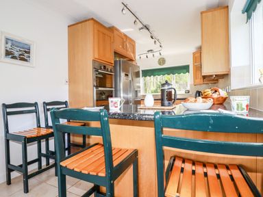 A kitchen with wooden cabinets, a stainless steel refrigerator, and dark green chairs at Trevow in Camborne