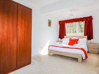 A bedroom with a double bed red curtains wooden wardrobe and bedside tables at Trevow in Camborne
