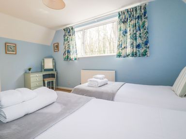 A bedroom with two single beds a dresser with a mirror and floral curtains at Trevow in Camborne