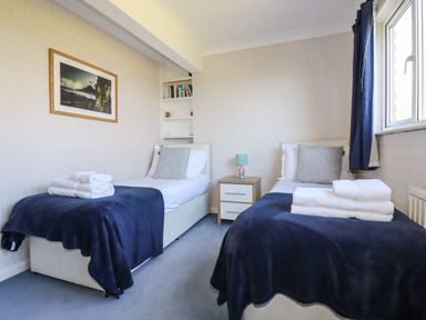 A bedroom with two single beds with navy blankets and towels on top and a window at Trevow Camborne