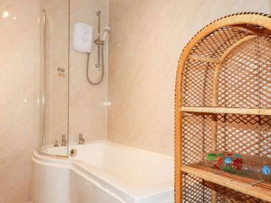 A bathroom with a bathtub shower combination and a wicker shelving unit with a plastic bath mat at Trevow in Camborne