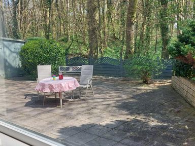 An outdoor patio with two chairs and a table with a pink tablecloth and drinks with trees and a fence in the background at Trevow Camborne