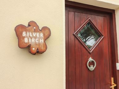 A wooden door with a diamond-shaped glass window and a metal knocker beside a wooden sign reading Silver Birch at Silver Birch in Dromelihy Cooraclare County Clare