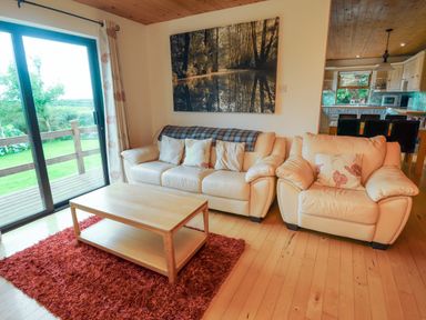 A living room with a leather sofa armchair wooden coffee table and large window at Silver Birch in Dromelihy Cooraclare County Clare