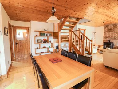 A dining area with a wooden table and black chairs next to wooden stairs and a living room with a fireplace at Silver Birch in Dromelihy Cooraclare County Clare