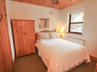 A bedroom with a double bed wooden wardrobe wooden ceiling and a window with patterned glass at Silver Birch in Dromelihy Cooraclare County Clare
