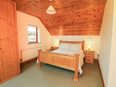 A bedroom with a wooden bed and matching bedside tables with lamps under a wooden ceiling at Silver Birch in Dromelihy Cooraclare County Clare