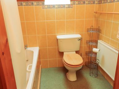 A bathroom with a toilet wooden seat bathtub with shower curtain and metal shelving unit at Silver Birch in Dromelihy Cooraclare County Clare