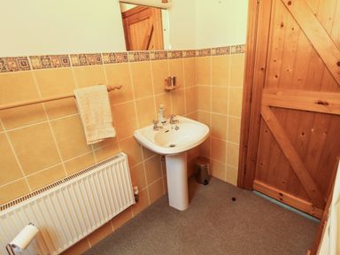 A bathroom with a wooden door a pedestal sink a towel on a rack a radiator and a small trash can at Silver Birch in Dromelihy Cooraclare County Clare