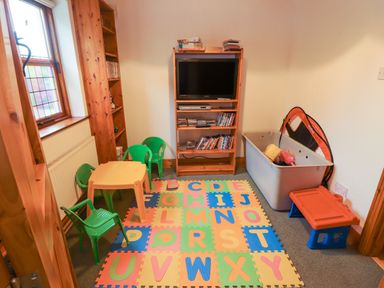 A children's playroom with a TV on a wooden stand alphabet foam mat small table with green chairs and a toy box at Silver Birch in Dromelihy Cooraclare County Clare