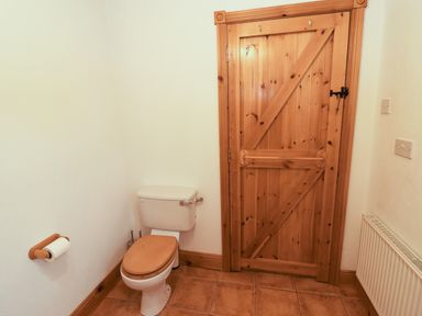 A bathroom with a toilet wooden door and tiled floor at Silver Birch in Dromelihy Cooraclare County Clare