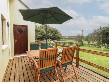 An outdoor wooden deck with a table umbrella and chairs overlooking a grassy area at Silver Birch in Dromelihy Cooraclare County Clare