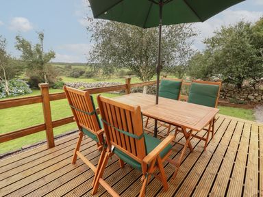 A wooden outdoor deck with a table and four chairs with green cushions under a green umbrella at Silver Birch in Dromelihy Cooraclare County Clare