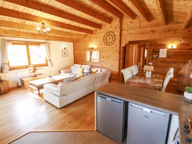 A living area with a white sectional sofa wooden tables a dining table with chairs and wooden walls at Jemima Lodge in Tattershall