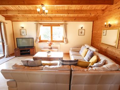 A living room with leather sofas cushions a wooden coffee table television and window at Jemima Lodge in Tattershall