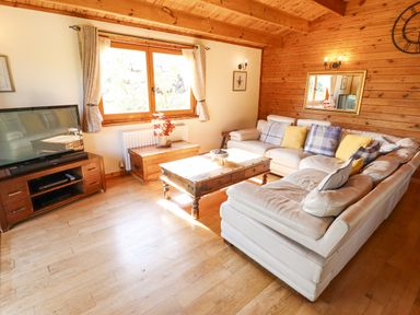 A living room with a white sectional sofa yellow and plaid cushions wooden coffee table a TV on wooden stand and window at Jemima Lodge in Tattershall