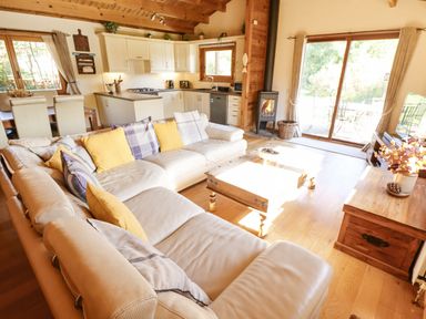 A living room with a beige sectional sofa and yellow and plaid pillows a wooden coffee table a wood stove kitchen cabinetry and dining area with windows at Jemima Lodge in Tattershall