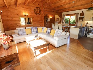 A living room with a white sectional sofa and wooden coffee table adjacent to a dining area and kitchen at Jemima Lodge in Tattershall