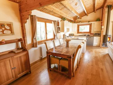A dining area with a wooden table and beige chairs beside a kitchen with white cabinets and a wood burning stove at Jemima Lodge in Tattershall