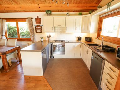 A kitchen with white cabinets a gas stove a dishwasher a sink and wooden dining table at Jemima Lodge in Tattershall
