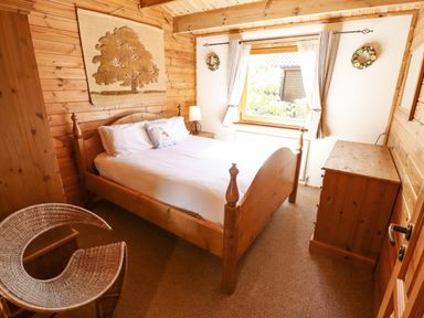 A bedroom with a wooden bed white bedding a wooden chest of drawers and a wicker chair at Jemima Lodge in Tattershall