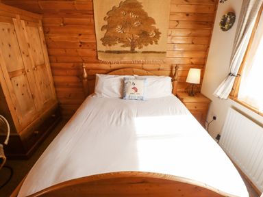 A bedroom with a wooden bed white bedding a wooden wardrobe and bedside table with lamp at Jemima Lodge in Tattershall