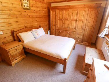 A bedroom with a wooden bed white bedding wooden wardrobe bedside table and chest at Jemima Lodge in Tattershall