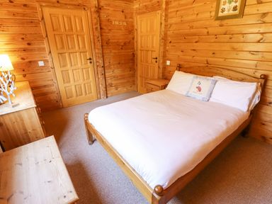 A bedroom with a wooden bed and white bedding with wooden doors and furniture at Jemima Lodge in Tattershall