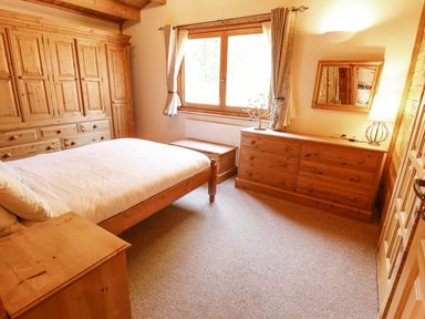 A bedroom with wooden furniture including a bed a wardrobe a dresser and a window at Jemima Lodge in Tattershall