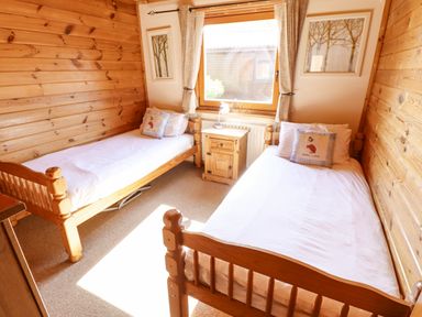 A bedroom with two single wooden beds a wooden nightstand between them and a window at Jemima Lodge in Tattershall