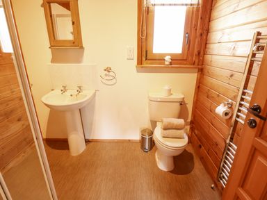 A bathroom with a pedestal sink a toilet with towels and a window with wooden panel walls at Jemima Lodge in Tattershall