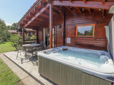 An outdoor patio with a hot tub and a metal table with chairs next to a wooden cabin at Jemima Lodge in Tattershall