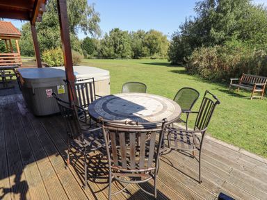 A patio with a round table and six chairs next to a hot tub and a grassy yard with trees and a bench at Jemima Lodge in Tattershall