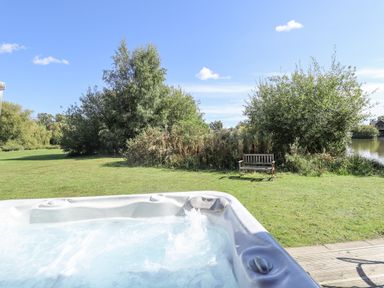 An outdoor hot tub with bubbles near a grassy area with trees and a bench by a lake at Jemima Lodge in Tattershall