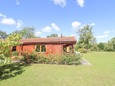 A wooden cabin with a red tiled roof and small shrubs in front on a grassy area with trees in the background at Jemima Lodge in Tattershall