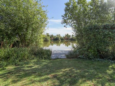 A small wooden dock leading to a lake surrounded by trees and grass at Jemima Lodge in Tattershall