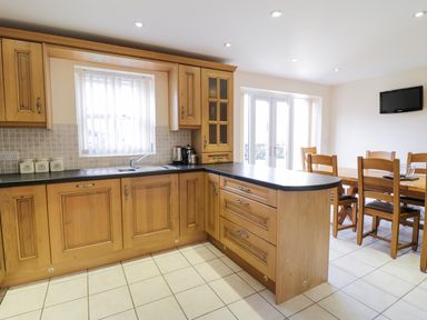 A kitchen with wooden cabinets and black countertops adjacent to a dining area with wooden table and chairs at Tyn Y Buarth in Dyffryn Ardudwy
