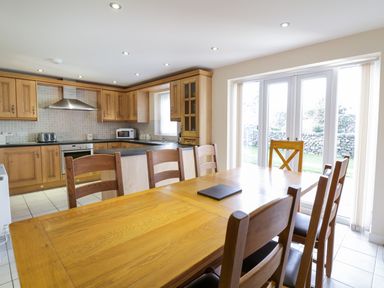 A kitchen and dining area with wooden cabinets and chairs near glass patio doors at Tyn Y Buarth in Dyffryn Ardudwy