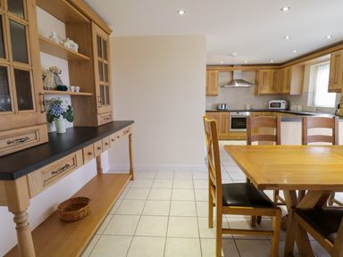 A kitchen with wooden cabinets a dining table and chairs and a sideboard with decorative items at Tyn Y Buarth in Dyffryn Ardudwy