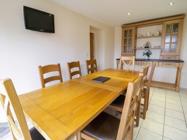 A dining room with a wooden table and chairs a wall mounted TV and a wooden cabinet at Tyn Y Buarth in Dyffryn Ardudwy