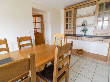 A dining room with a wooden table and chairs a wooden cabinet with shelves and decorative items at Tyn Y Buarth in Dyffryn Ardudwy
