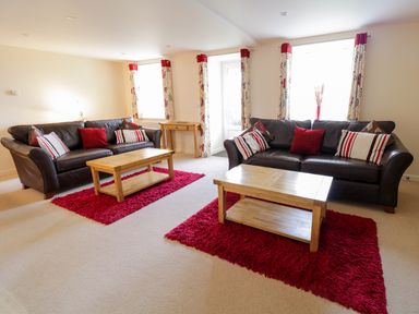 A living room with two brown leather sofas red cushions wooden coffee tables and patterned curtains at Tyn Y Buarth in Dyffryn Ardudwy