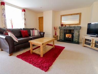 A living room with a brown leather sofa red rug wooden coffee table stone fireplace and television at Tyn Y Buarth in Dyffryn Ardudwy