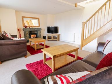 A living room with leather sofas wooden tables fireplace and a television at Tyn Y Buarth in Dyffryn Ardudwy